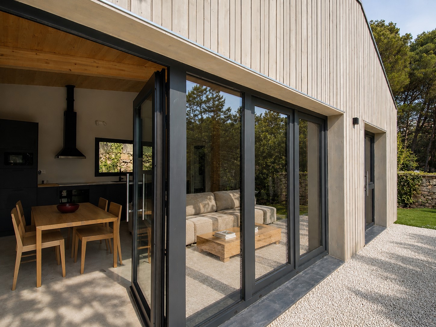 Acceso exterior de vivienda en Canyelles con carpinterías de aluminio oscuras y fachada de madera